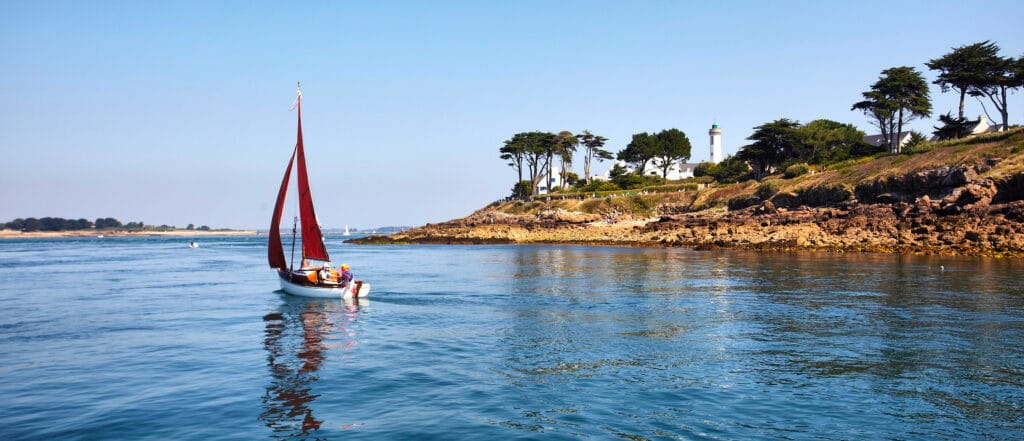 Voilier aux voiles rouges devant le phare de Port-Navalo, à l’entrée du golfe du Morbihan