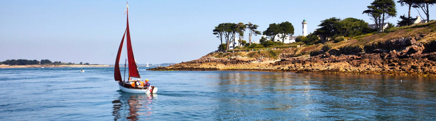 Voilier aux voiles rouges devant le phare de Port-Navalo, à l’entrée du golfe du Morbihan